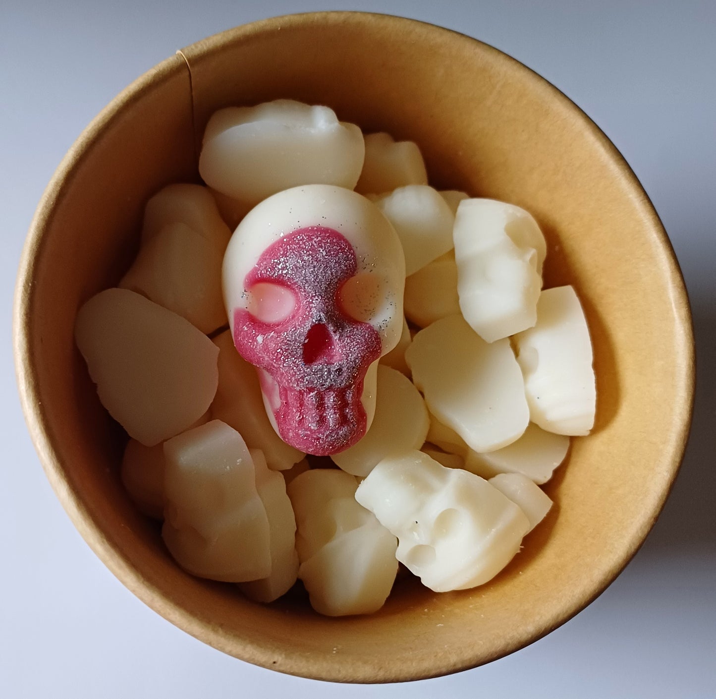 White wax melts with a red centre in a brown paper cup on a light grey background