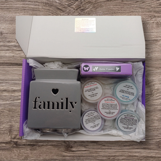 Gift set with 'family' burner, baby powder wax melts, and other products in a box on a wooden surface.