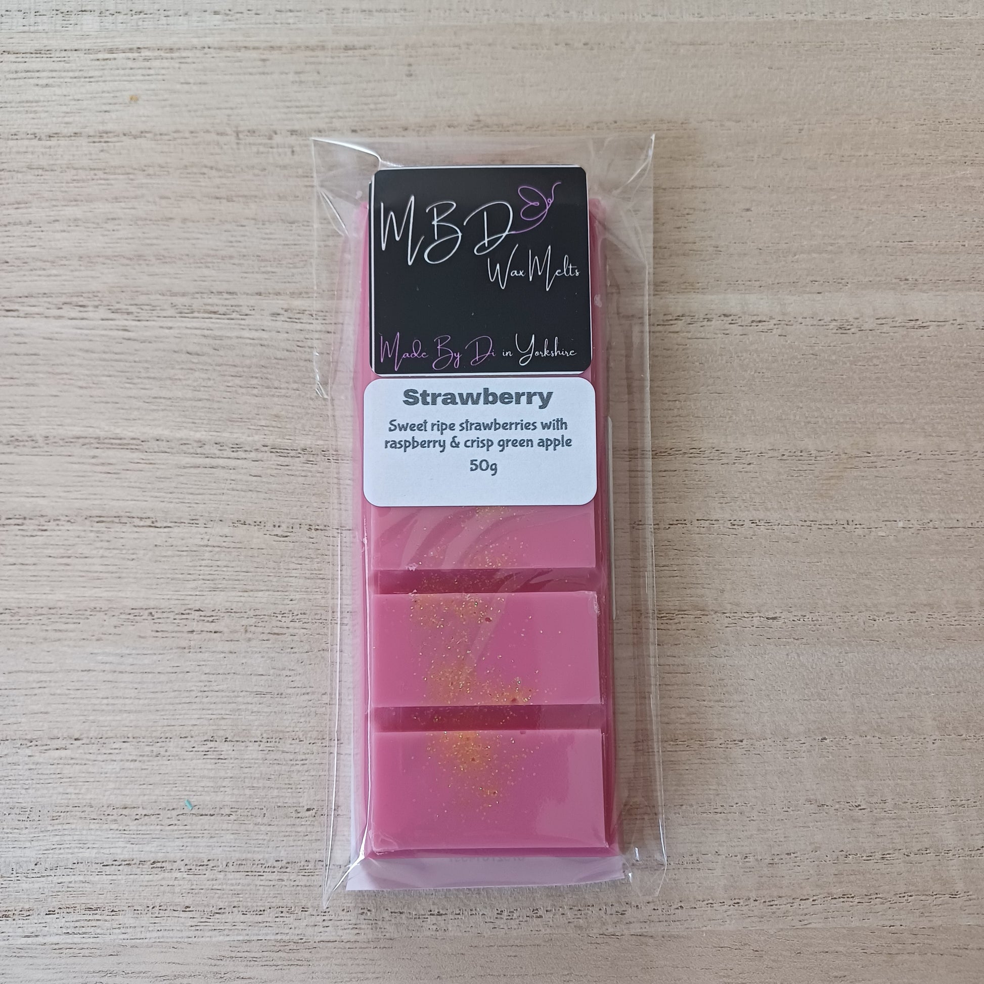 Pink wax melt bar in clear packaging with a label on a beige surface