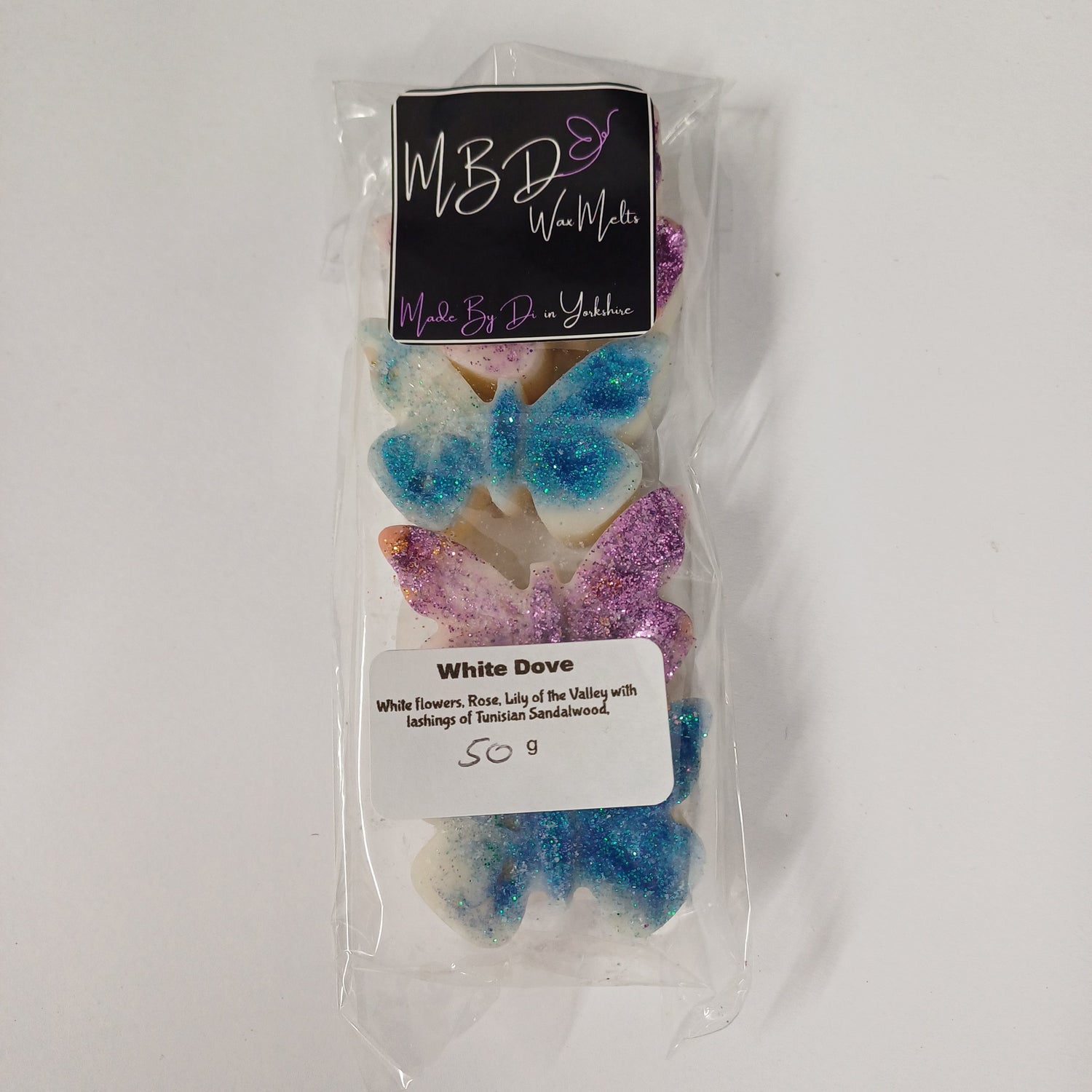 Packaged butterfly-shaped wax melts with colourful glitter on a white background