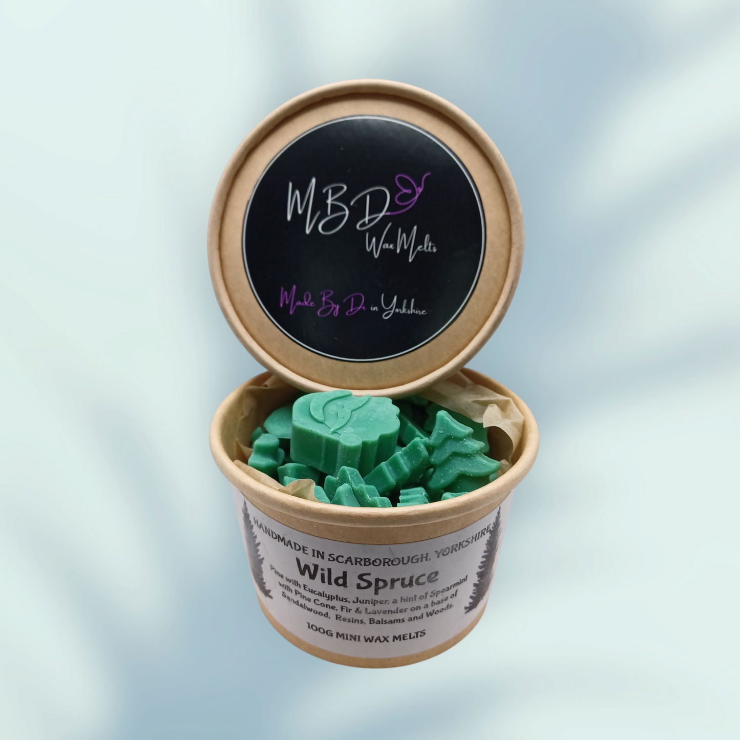 Open container of green wax melts with a branded lid on a light blue background